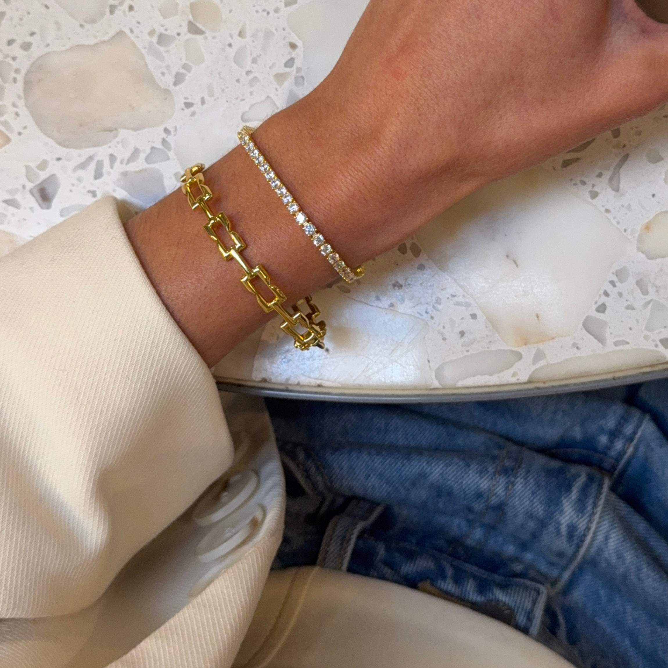 Close-up of a wrist wearing the LAVANA Signature Gold Bracelet and the Roland Gold Diamond Tennis Bracelet, resting on a marble table.