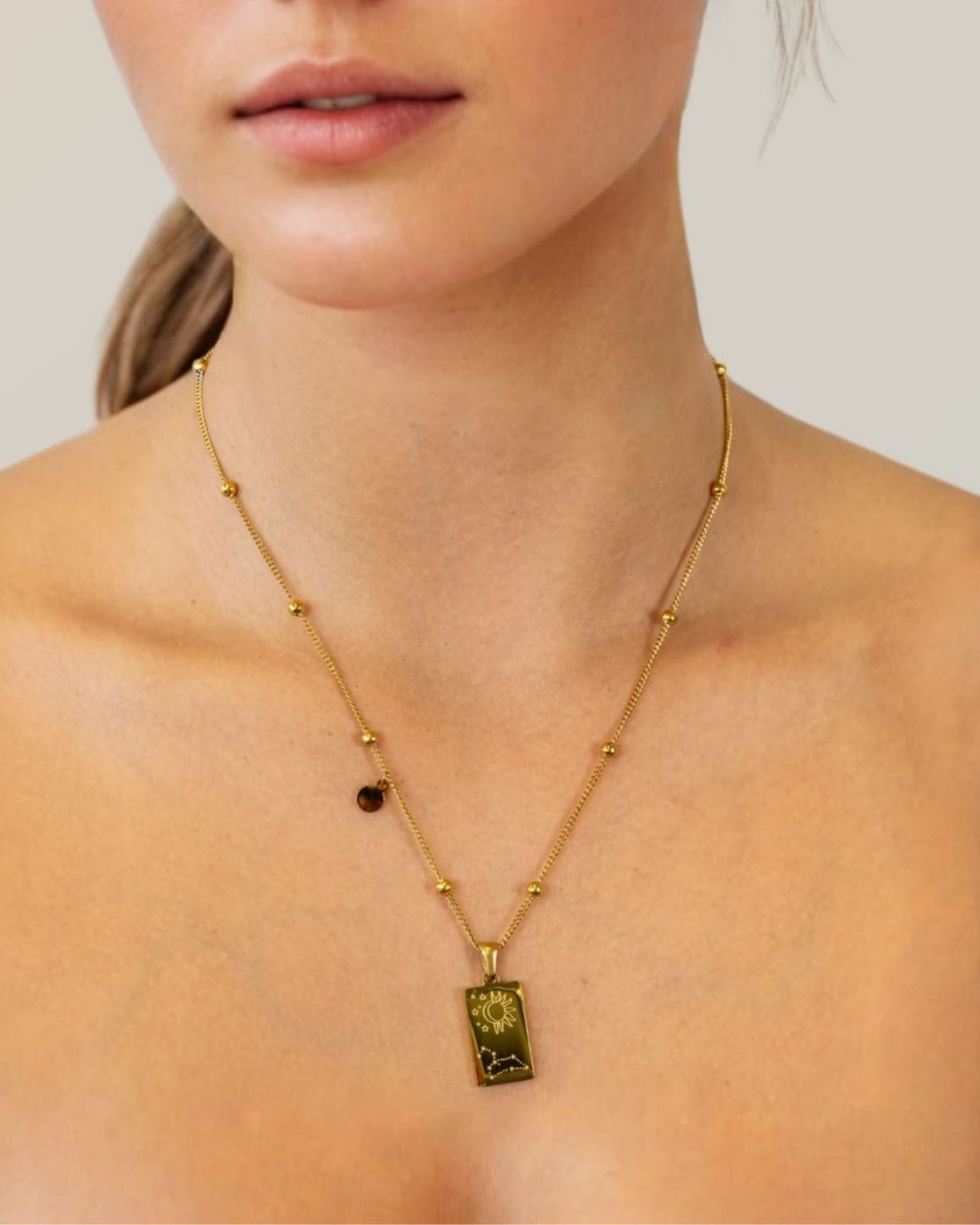 Leo Gold Zodiac Tag Necklace by Lavana, on model; engraved tag with constellation on beaded chain, back