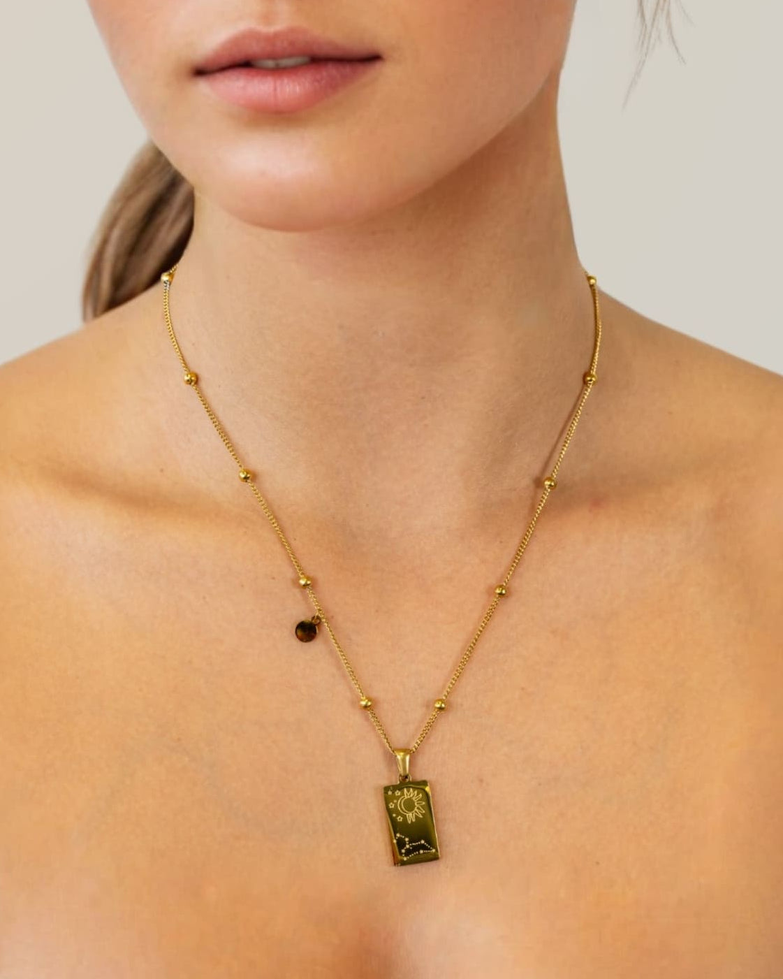 Leo Gold Zodiac Tag Necklace by Lavana, on model; engraved tag with constellation on beaded chain, back