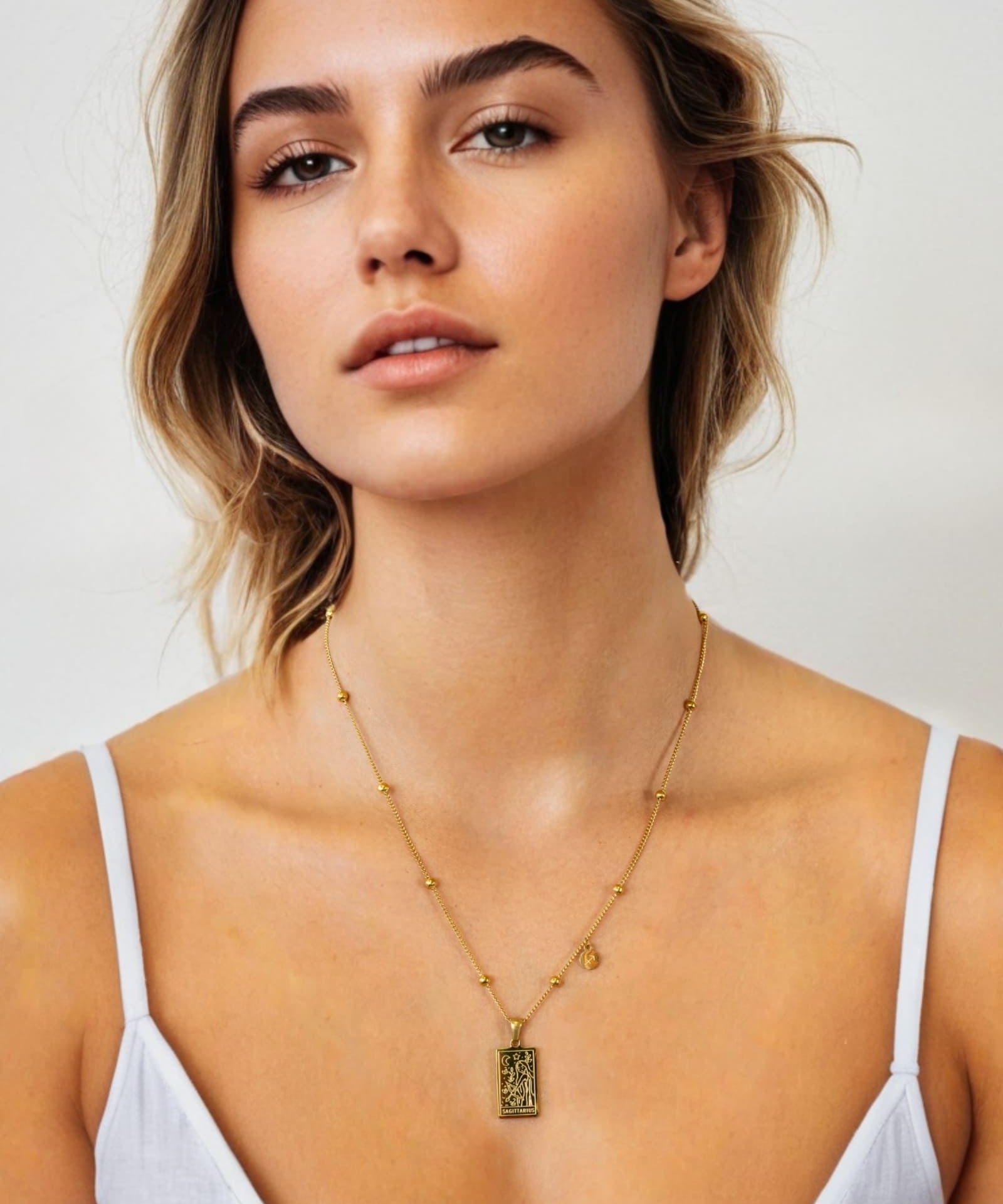 Sagittarius Gold Zodiac Tag Necklace by Lavana, on model; engraved tag on beaded chain, front