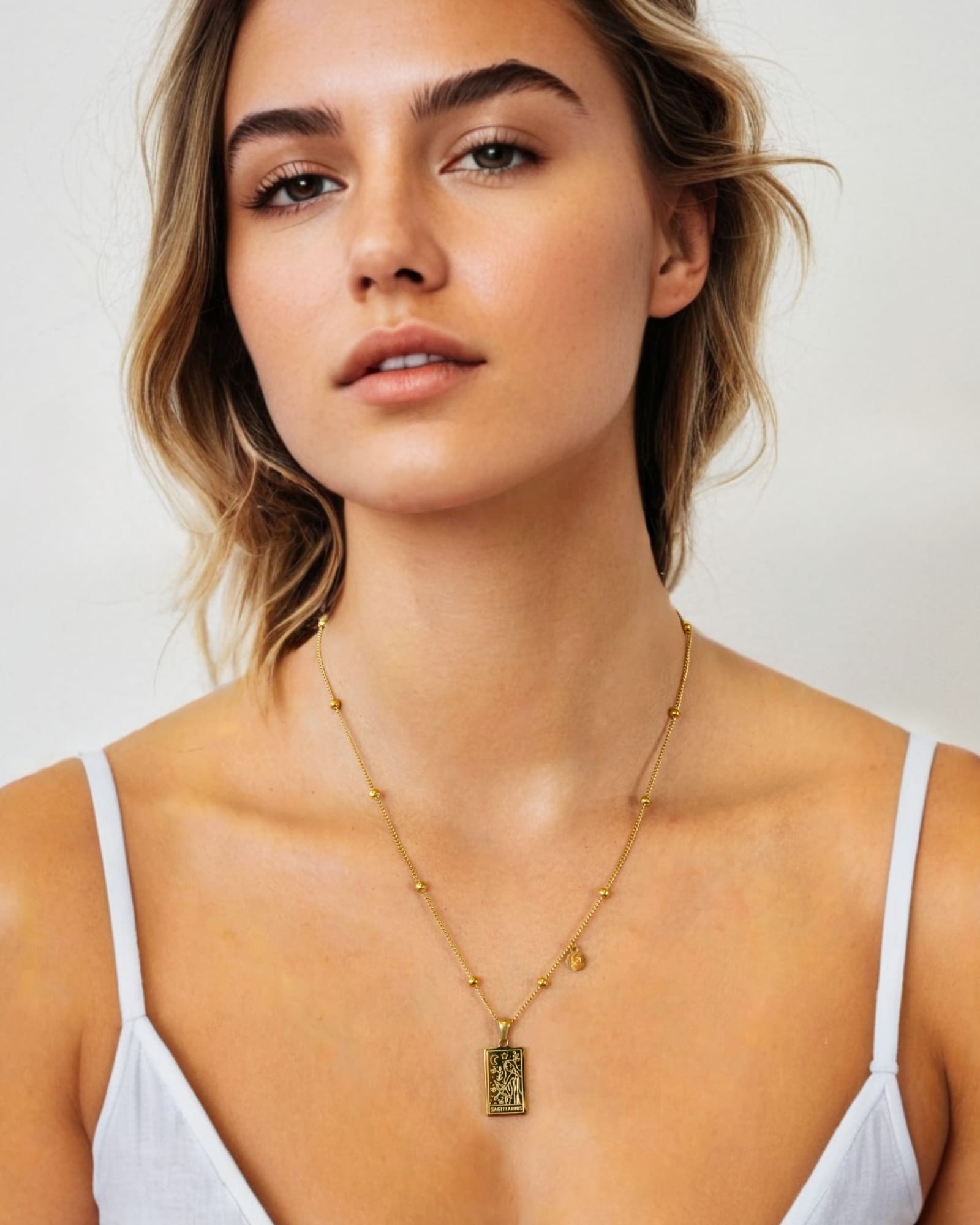 Sagittarius Gold Zodiac Tag Necklace by Lavana, on model; engraved tag on beaded chain, front