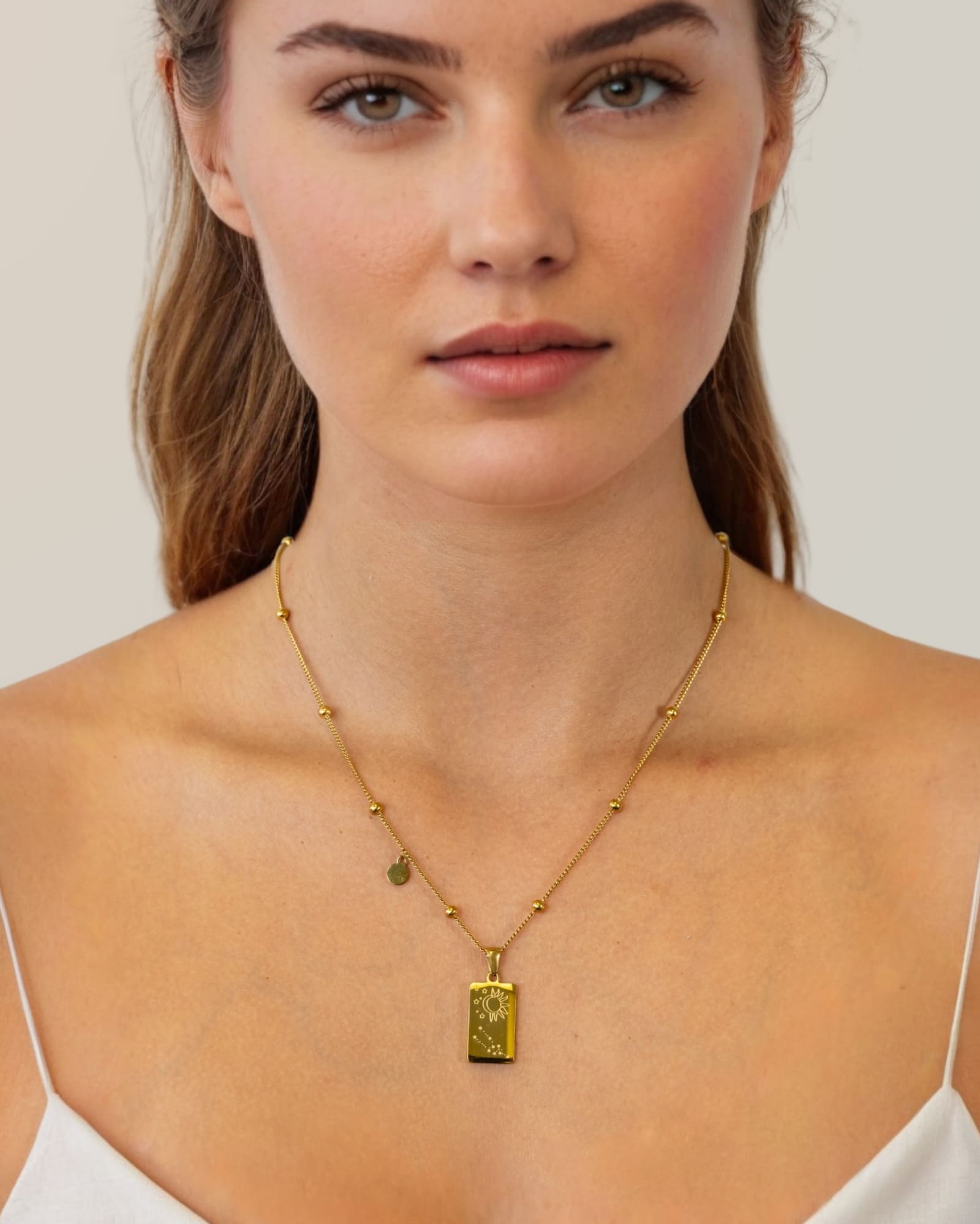 Taurus Gold Zodiac Tag Necklace by Lavana, on model; engraved tag with constellation on beaded chain, back