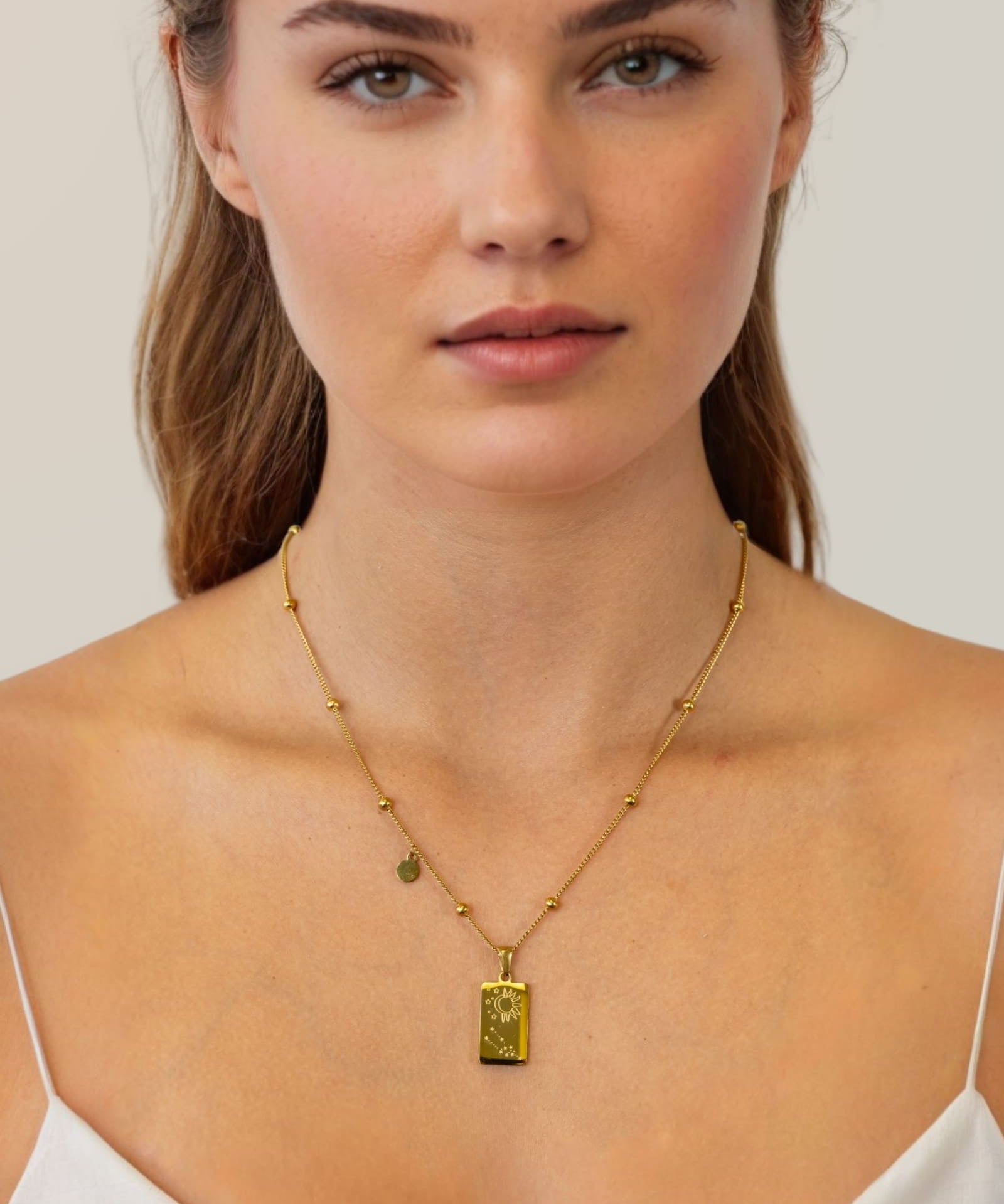 Taurus Gold Zodiac Tag Necklace by Lavana, on model; engraved tag with constellation on beaded chain, back